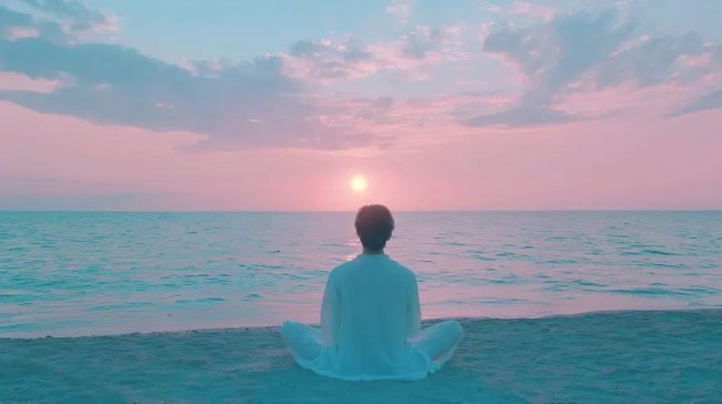 Man meditating on beach at sunrise.